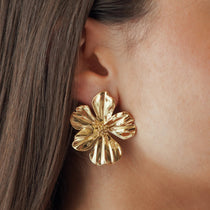 Boucles d'oreilles grand format forme fleur épanouie en acier inoxydable doré portées à l'oreille, style statement.