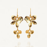 Gros plan boucles d'oreilles pendantes avec double motif floral doré sur fond blanc.