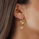 Boucles d'oreilles pendantes motif fleurs en cascade en acier inoxydable doré portées à l'oreille.