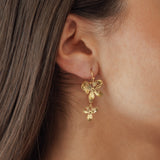 Boucles d'oreilles pendantes motif fleurs en cascade en acier inoxydable doré portées à l'oreille.