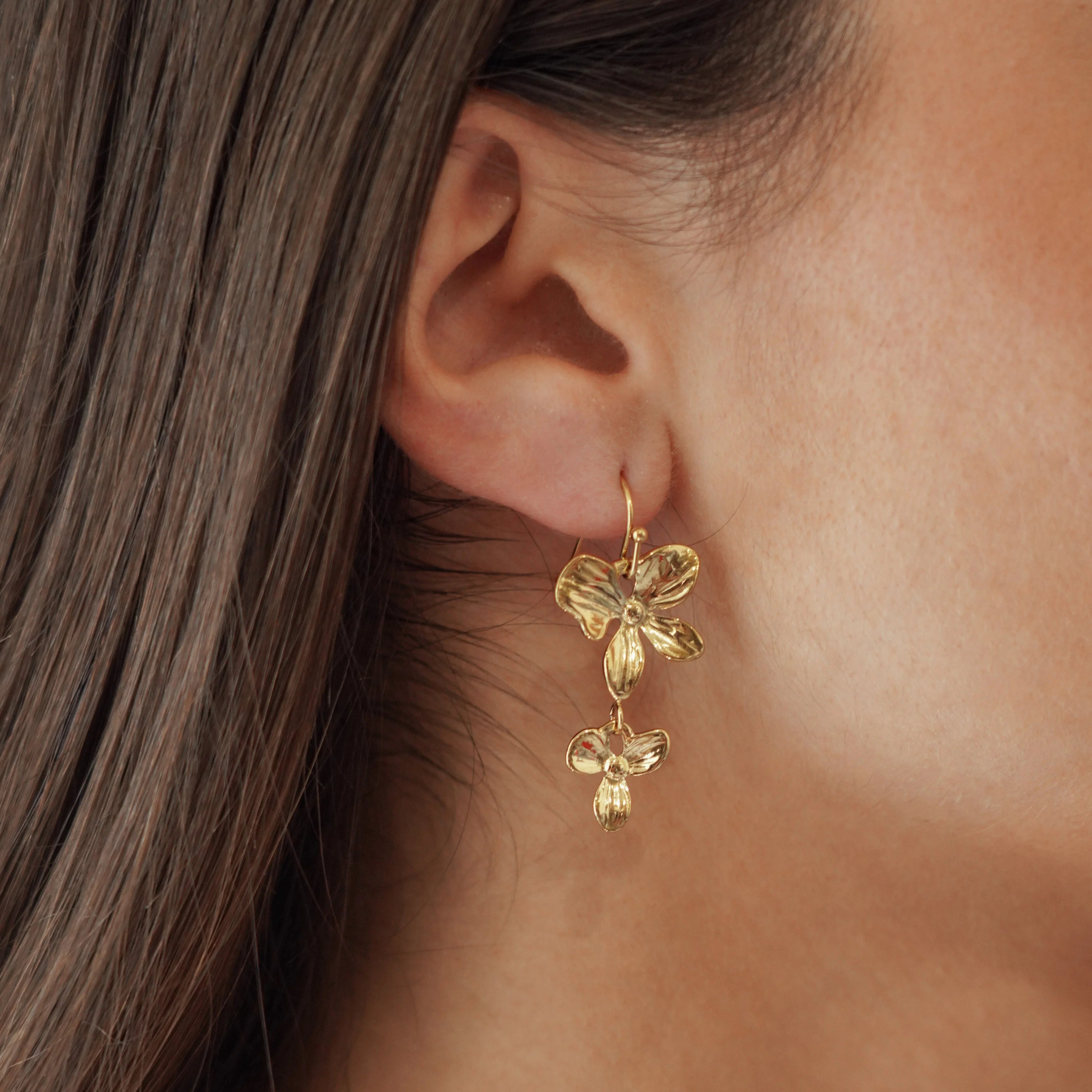 Boucles d'oreilles pendantes motif fleurs en cascade en acier inoxydable doré portées à l'oreille.