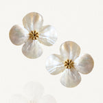 Paire de boucles d'oreilles puces motif fleur à quatre pétales blanc nacré et centre doré sur fond blanc.