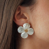 Boucles d'oreilles grand format fleur blanche aspect nacre avec cœur doré portées à l'oreille, idéal mariage ou cérémonie.