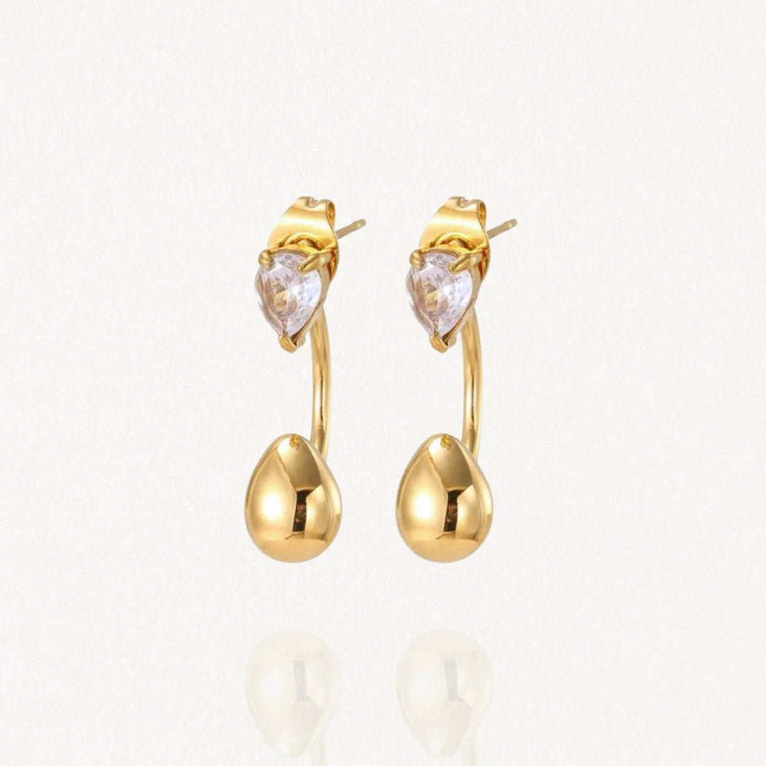 Boucles d'oreilles dessous de lobe (ear jackets) en acier inoxydable doré composées d'une puce strass et d'une goutte dorée pendante.