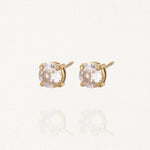 Paire de boucles d'oreilles puces solitaires en acier inoxydable doré avec pierre ronde brillante (zirconium) sur fond blanc.