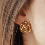 Boucles d'oreilles puces volumineuses forme nœud entrelacé en acier inoxydable doré portées à l'oreille.