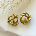 Paire de boucles d'oreilles Isabela motif nœud tubulaire vintage posées sur un décor naturel.