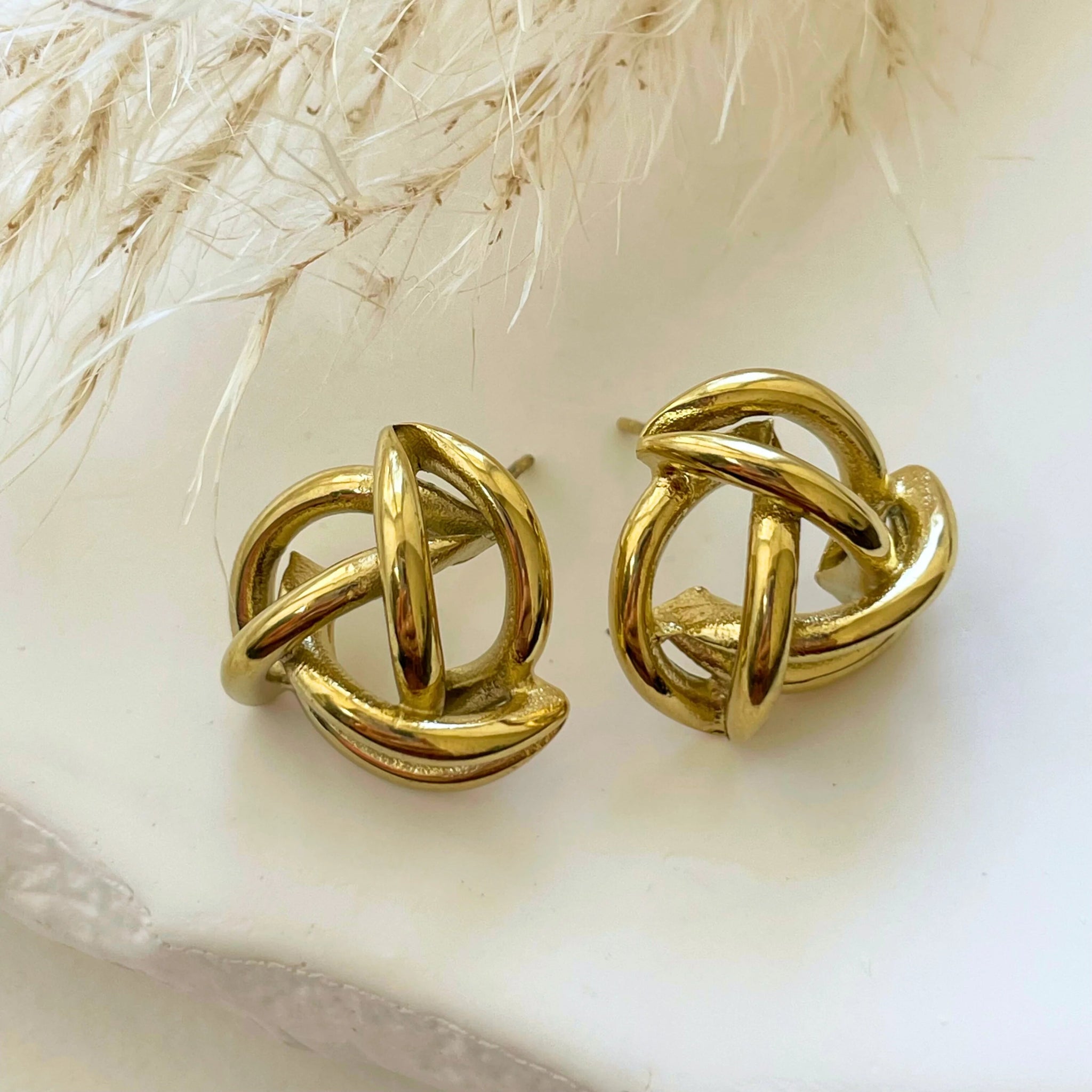 Paire de boucles d'oreilles Isabela motif nœud tubulaire vintage posées sur un décor naturel.