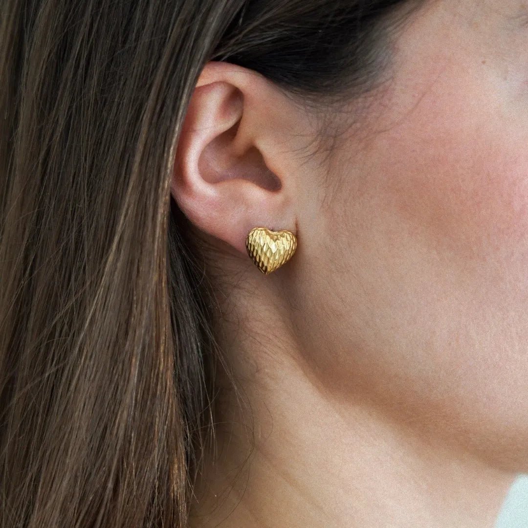 Boucle d'oreille clou cœur doré martelé portée sur l'oreille d'une femme aux cheveux bruns.