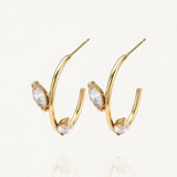 Paire de demi-créoles ouvertes en acier inoxydable doré ornées de deux cristaux taille marquise (ou navette) sur fond blanc.