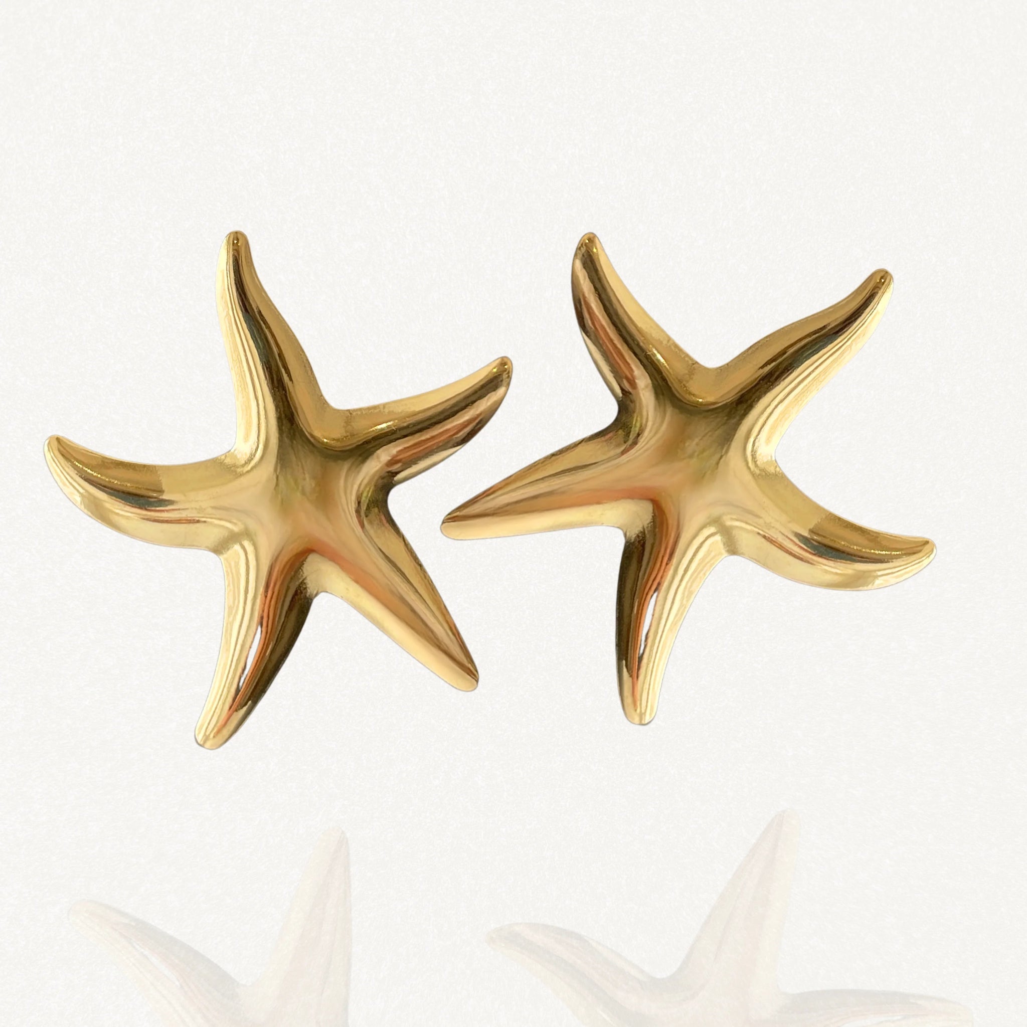 Paire de boucles d'oreilles Victoria forme étoile de mer dorée sur fond blanc.