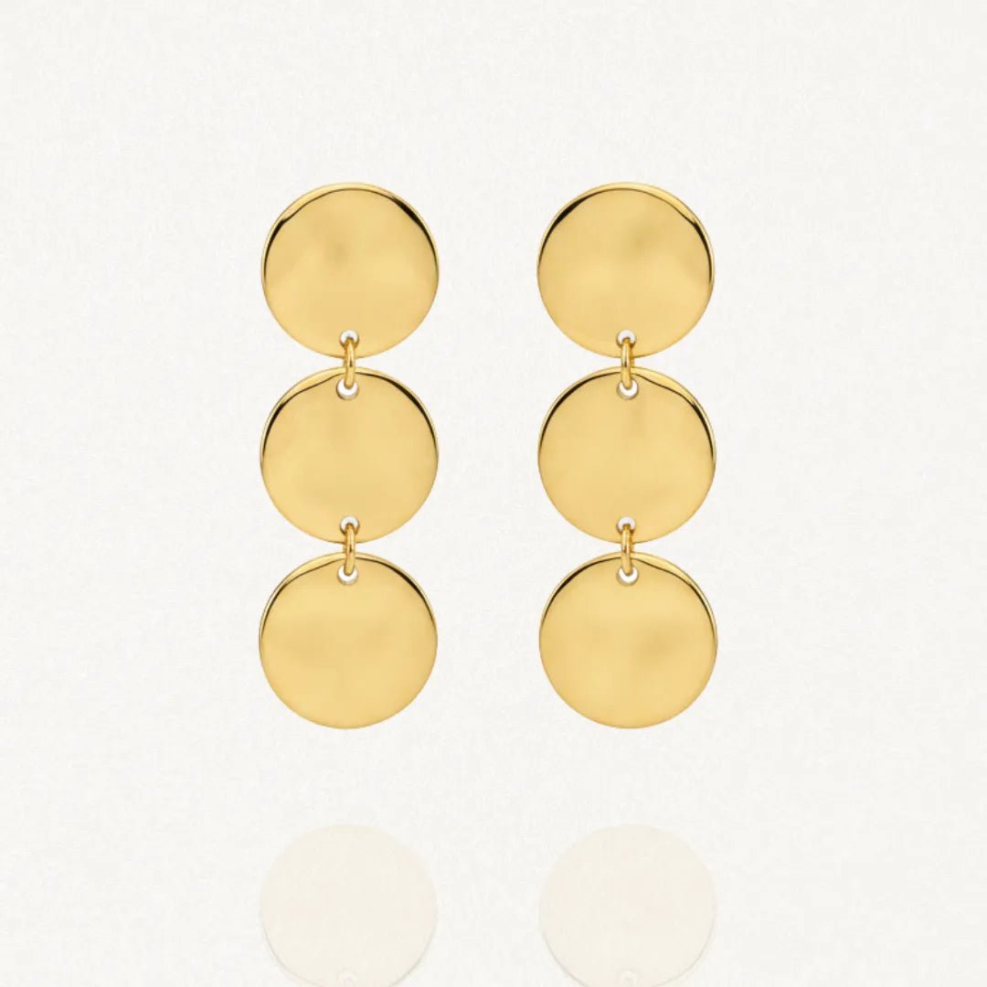 Deux boucles d'oreilles pendantes dorées sur un fond blanc. Chaque boucle est composée de trois disques ronds et plats, reliés verticalement par de petits anneaux.