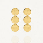Deux boucles d'oreilles pendantes dorées sur un fond blanc. Chaque boucle est composée de trois disques ronds et plats, reliés verticalement par de petits anneaux.