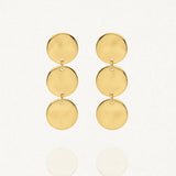 Deux boucles d'oreilles pendantes dorées sur un fond blanc. Chaque boucle est composée de trois disques ronds et plats, reliés verticalement par de petits anneaux.