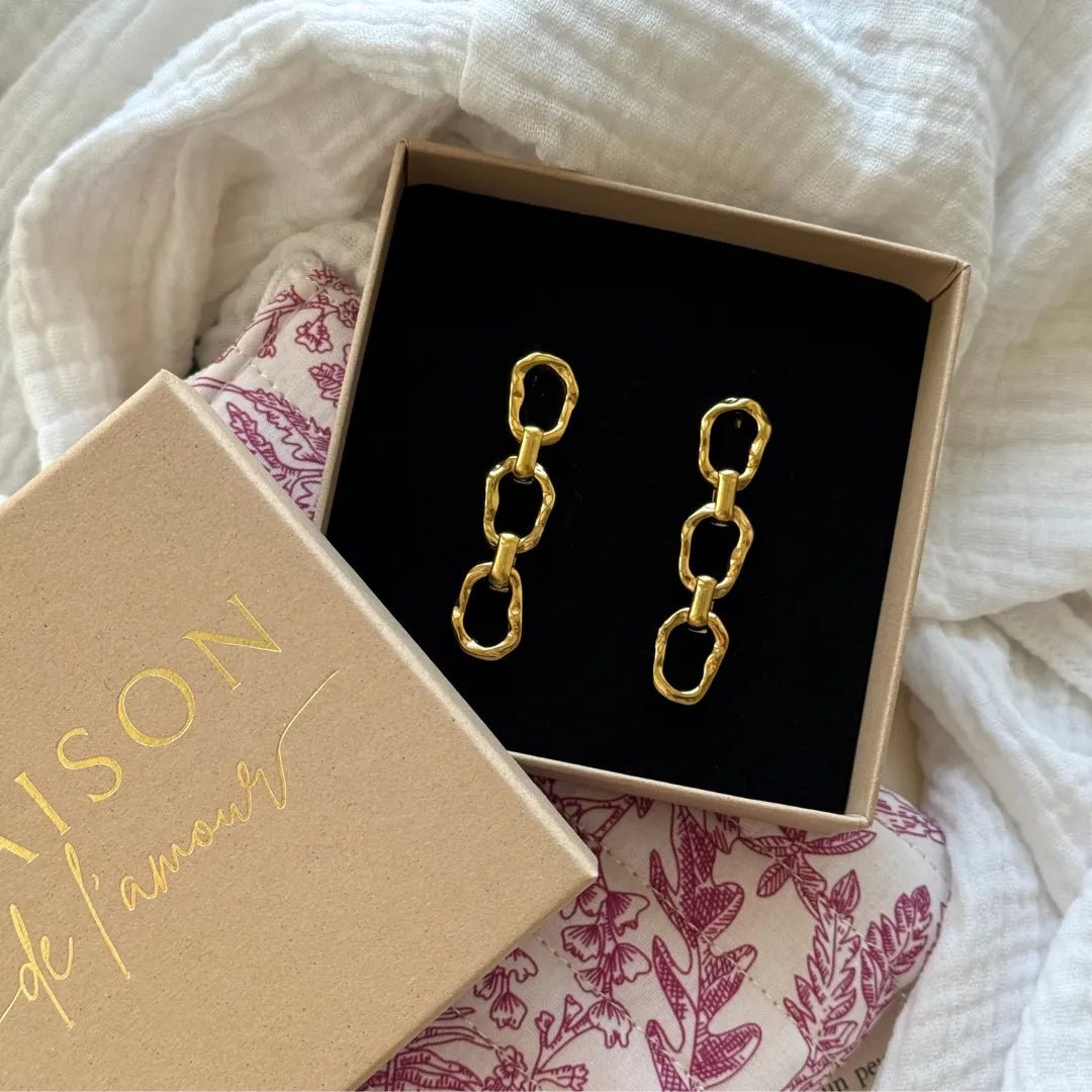 Boucles d'oreilles pendantes dorées 3 maillons organiques texturés, dans boîte beige ouverte Maison de l'amour.
