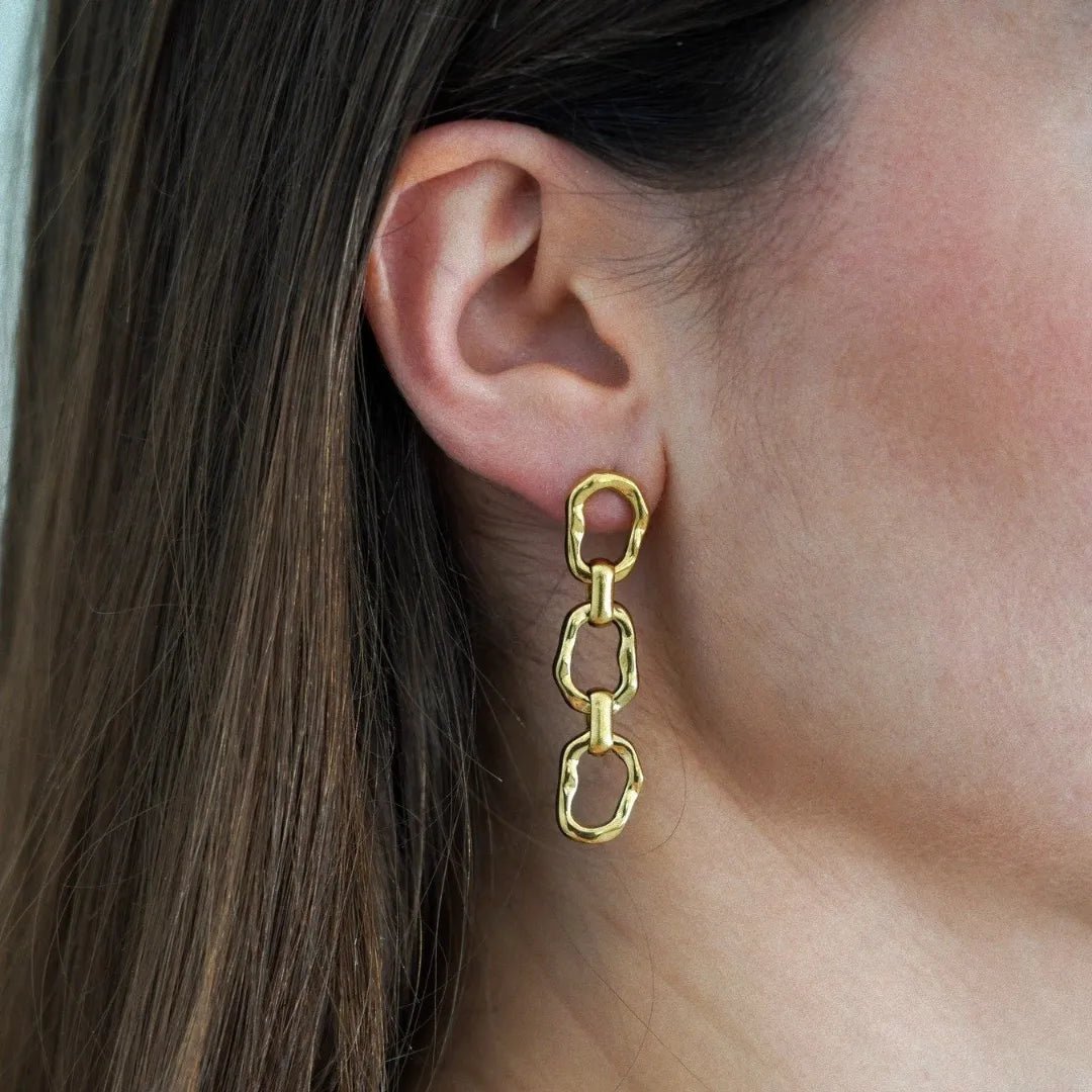 Boucle d'oreille pendante dorée, 3 maillons ovales irréguliers martelés, portée sur une oreille.