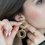 Femme aux longs ongles blancs ajustant boucle d'oreille pendante dorée, deux cercles ajourés motifs rayons, bague ondulée or.