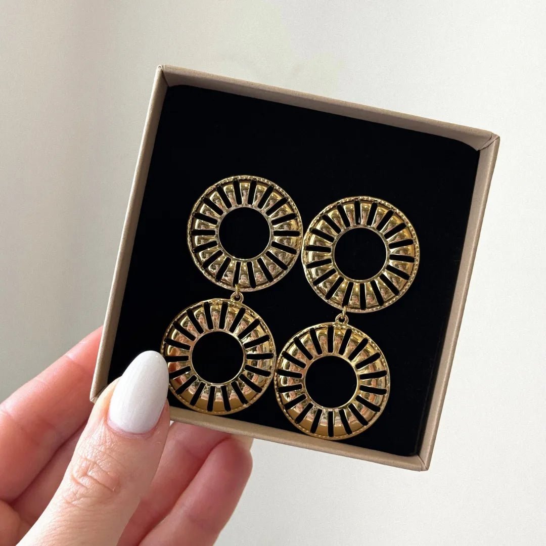 Main tient boîte cadeau avec 2 paires boucles d'oreilles dorées pendantes double cercle ajouré motif rayons sur velours noir.