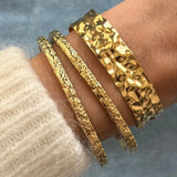 Accumulation de bracelets dorés : le jonc large Anouchka porté avec les joncs fins texturés Azalea.