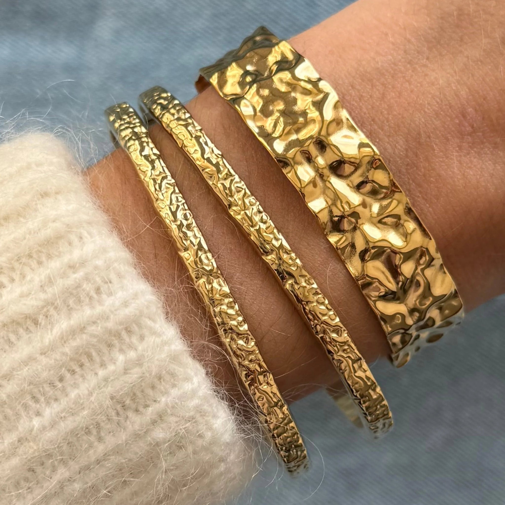 Accumulation de bracelets dorés : le jonc large Anouchka porté avec les joncs fins texturés Azalea.