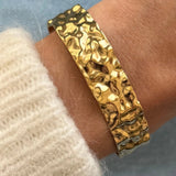 Gros plan bracelet jonc large Anouchka en acier inoxydable doré effet martelé porté au poignet.