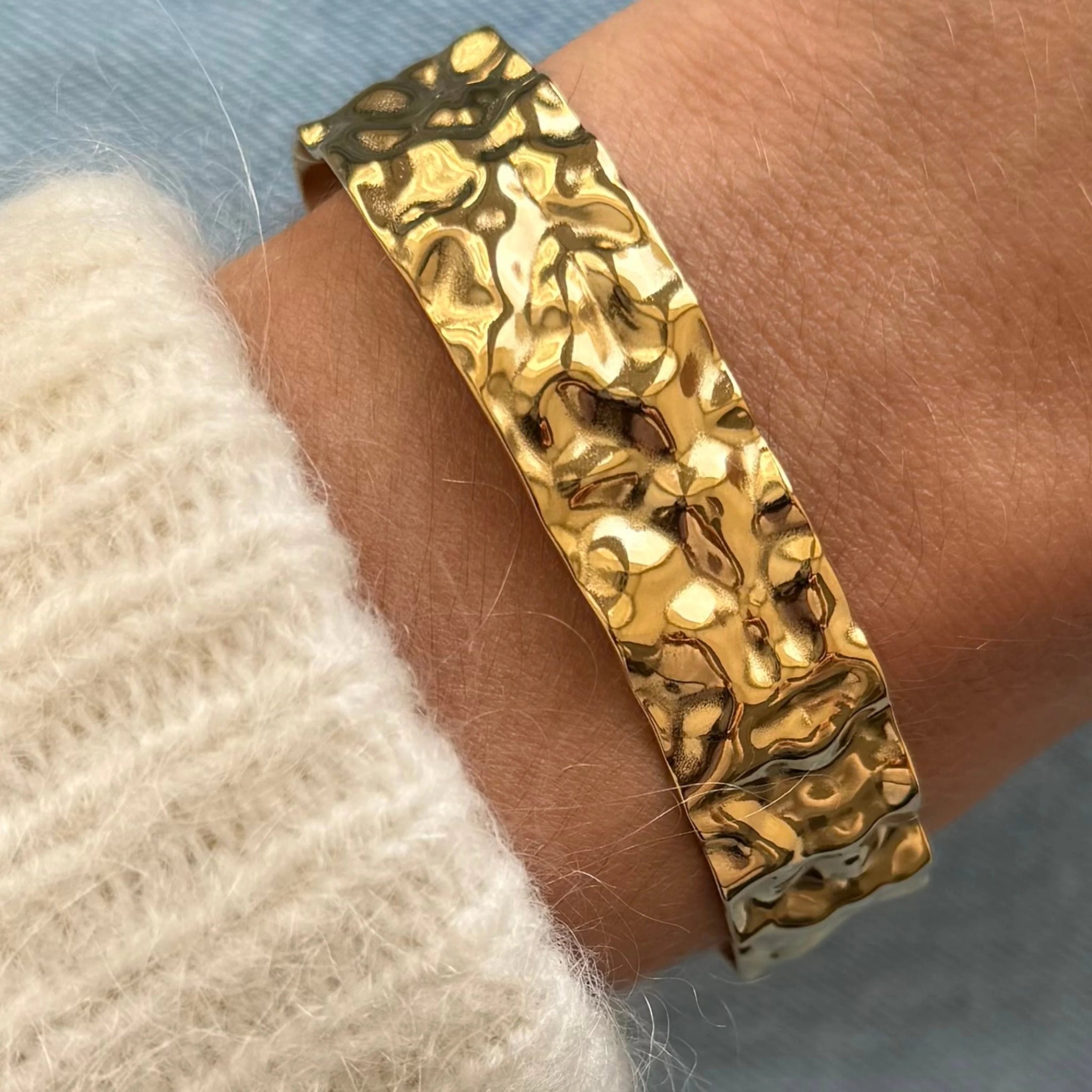 Gros plan bracelet jonc large Anouchka en acier inoxydable doré effet martelé porté au poignet.