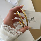 Duo de bracelets joncs Azalea dorés tenus en main, détail de la texture brute et lumineuse.