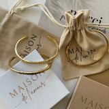 Bracelets joncs Azalea présentés avec leurs pochettes en tissu et boîtes cadeaux Maison de l'Amour.