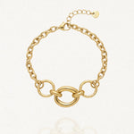 Bracelet en acier inoxydable doré composé de maillons épais et d'une section centrale avec un grand anneau ovale lisse encadré de deux anneaux ronds texturés. Fermoir mousqueton et chaînette d'extension.