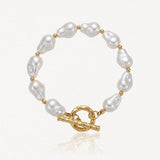Bracelet en acier inoxydable doré avec de grandes perles baroques blanches et un fermoir toggle martelé.
