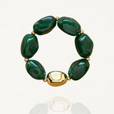 Vue de face sur fond blanc d'un bracelet élastique composé de perles vertes effet pierre et d'une grosse perle dorée lisse.