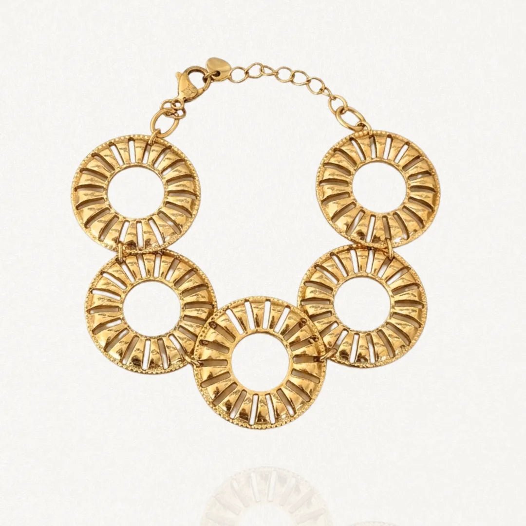Bracelet doré en acier inoxydable composé de cinq grands maillons ronds ajourés de style rayonnant, avec un fermoir mousqueton et une chaînette d'extension, sur fond blanc.