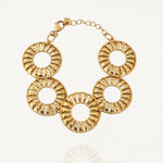 Bracelet doré en acier inoxydable composé de cinq grands maillons ronds ajourés de style rayonnant, avec un fermoir mousqueton et une chaînette d'extension, sur fond blanc.