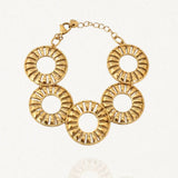 Bracelet doré en acier inoxydable composé de cinq grands maillons ronds ajourés de style rayonnant, avec un fermoir mousqueton et une chaînette d'extension, sur fond blanc.