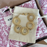 Bracelet doré à 5 maillons ronds ajourés motif soleil, posé sur pochette beige dans un emballage cadeau floral rose et marron.