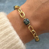 Bracelet grosse maille en acier inoxydable doré alterné avec des perles cylindriques effet pierre naturelle vert foncé porté au poignet.