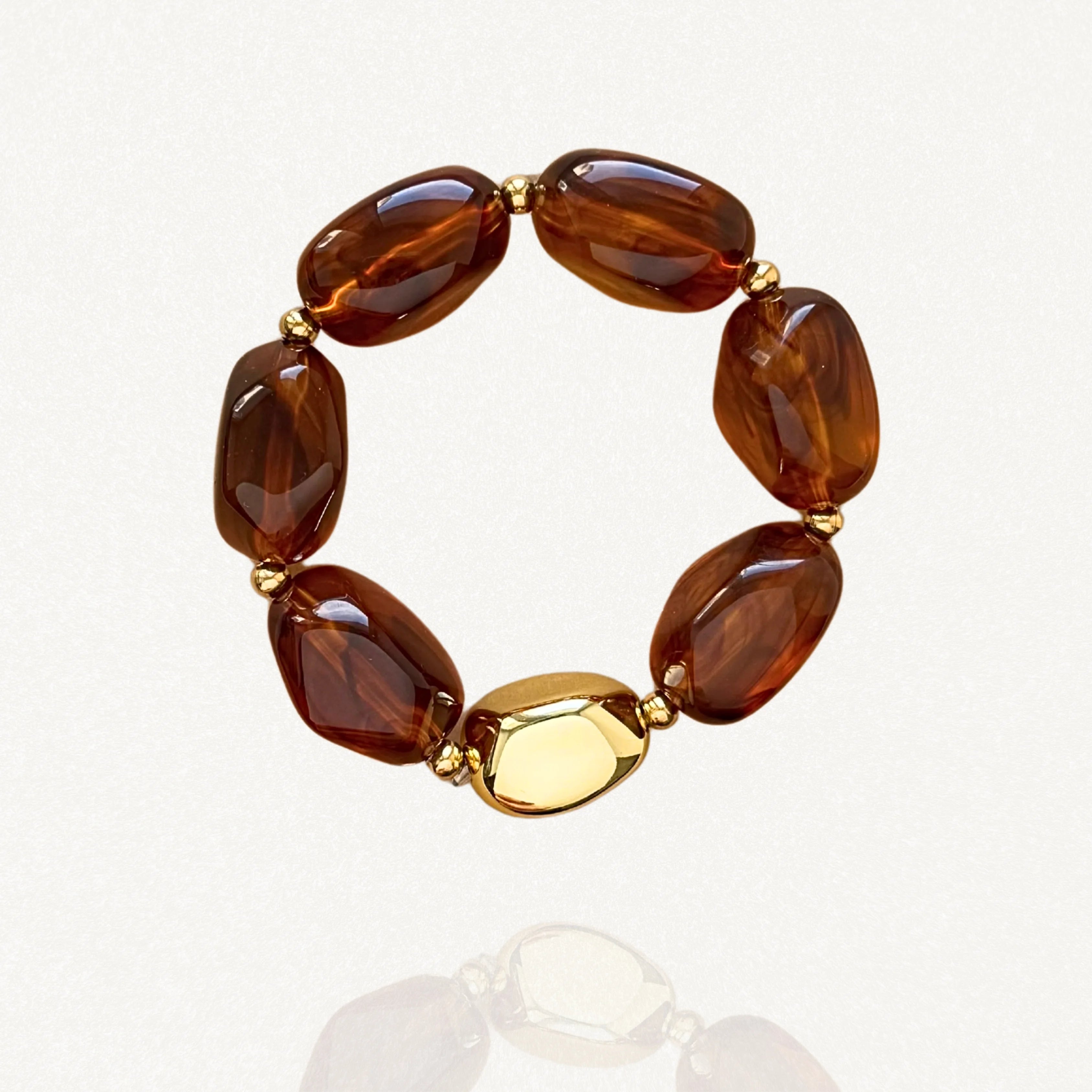Bracelet élastique femme composé de grosses perles marron effet ambre et d'une perle centrale dorée sur fond blanc.