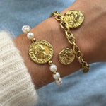 Bracelet perles et médaille Heloise porté en accumulation (stacking) avec un bracelet chaîne dorée à breloques.