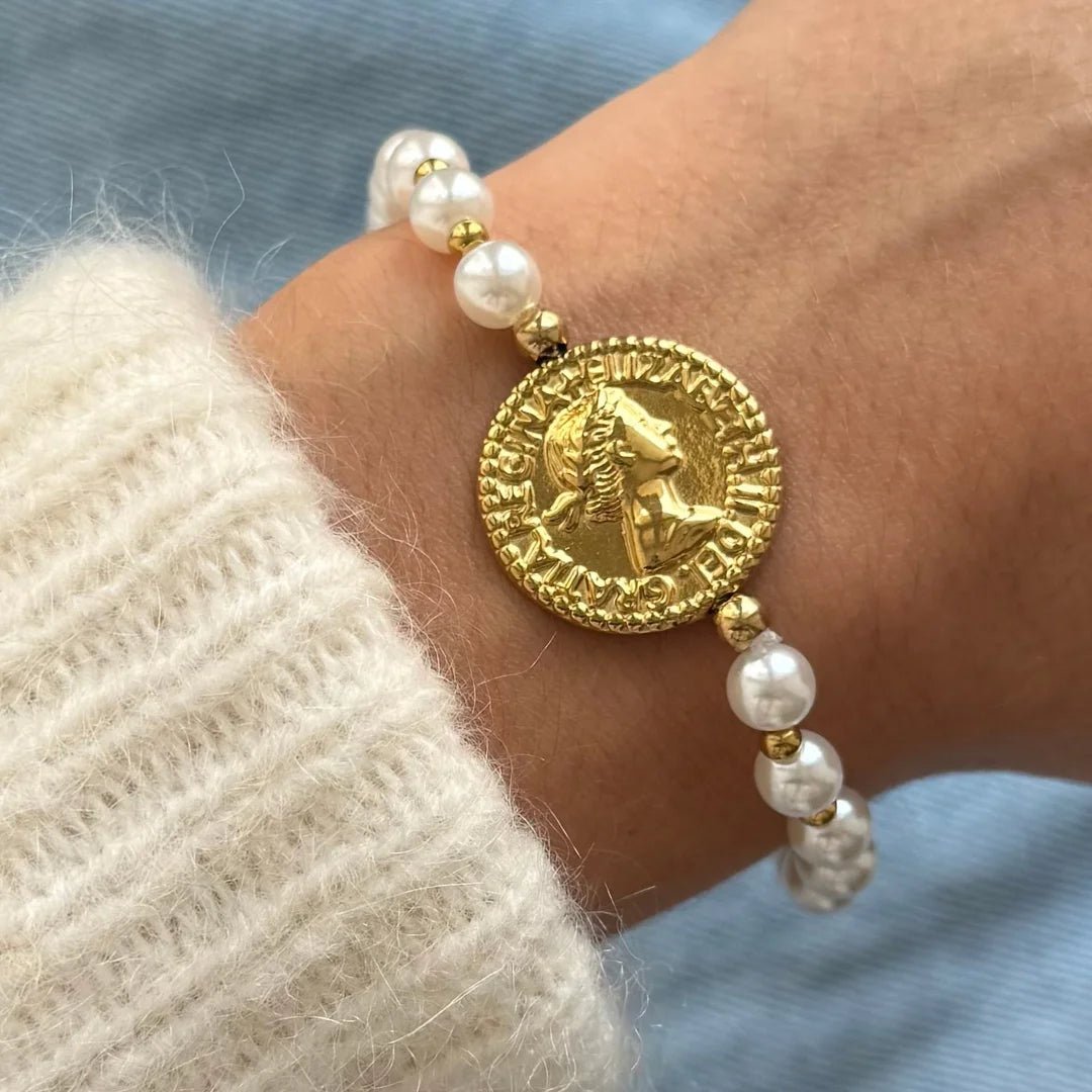 Gros plan bracelet perles blanches et petites billes dorées avec médaillon central pièce de monnaie antique porté au poignet.