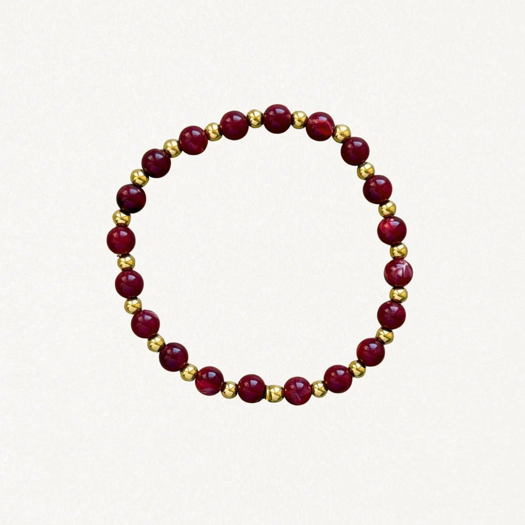 Bracelet fin perles bordeaux et billes dorées sur fond blanc.