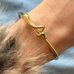 Aperçu du bracelet jonc doré fin porté au poignet, mettant en valeur le design du nœud sur la peau.