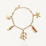 Vue d'ensemble bracelet doré à multiples pendentifs marins : hippocampe, étoile de mer, corail et coquillage sur fond blanc.