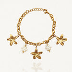 Vue d'ensemble bracelet chaîne doré avec multiples pendentifs fleurs dorées et fleurs en perles sur fond blanc.