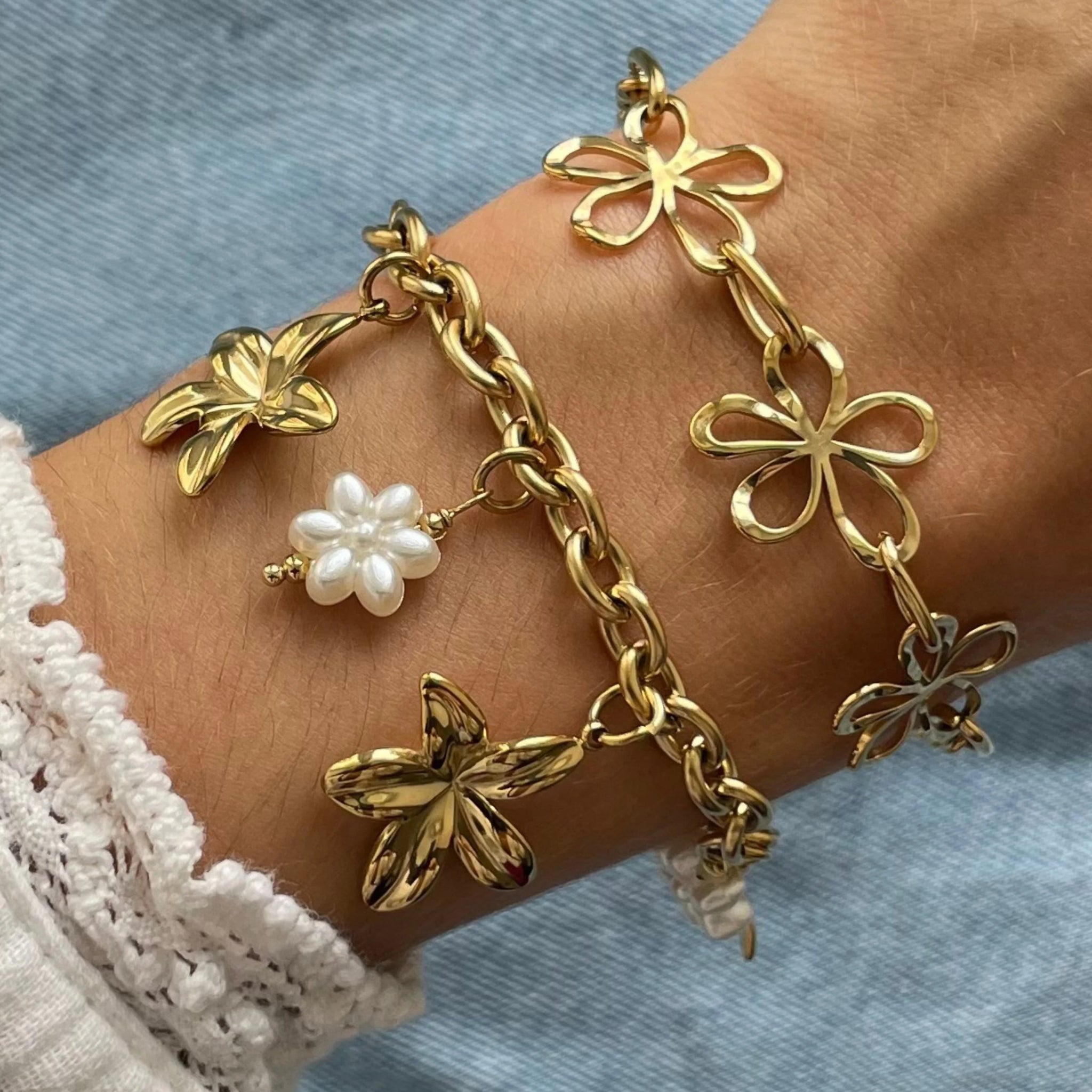Bracelet à breloques fleurs Marga porté en accumulation (stacking) avec un autre bracelet chaîne à motifs floraux ajourés.