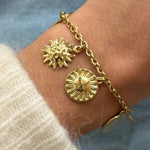 Gros plan bracelet chaîne en acier inoxydable doré avec breloques soleils et médailles texturées porté au poignet.