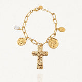 Bracelet MARIE-PIERRE en acier inoxydable doré, composé d'une chaîne à maillons ovales et de quatre pendentifs : une croix texturée, deux médaillons ronds gravés et une petite pierre de zircon transparente en forme de goutte. Le bracelet est posé sur un fond blanc légèrement texturé.