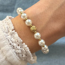 Bracelet de perles blanches, billes dorées et perle centrale dorée sculptée, porté sur un poignet avec manche en dentelle.