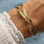 Gros plan bracelet jonc ouvert rigide Nyla en acier inoxydable doré avec design croisé et entrelacé porté au poignet.