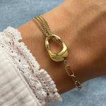 Gros plan bracelet asymétrique Olga en acier inoxydable doré : mélange de chaînes fines multi-rangs et maillons larges avec pendentif organique.