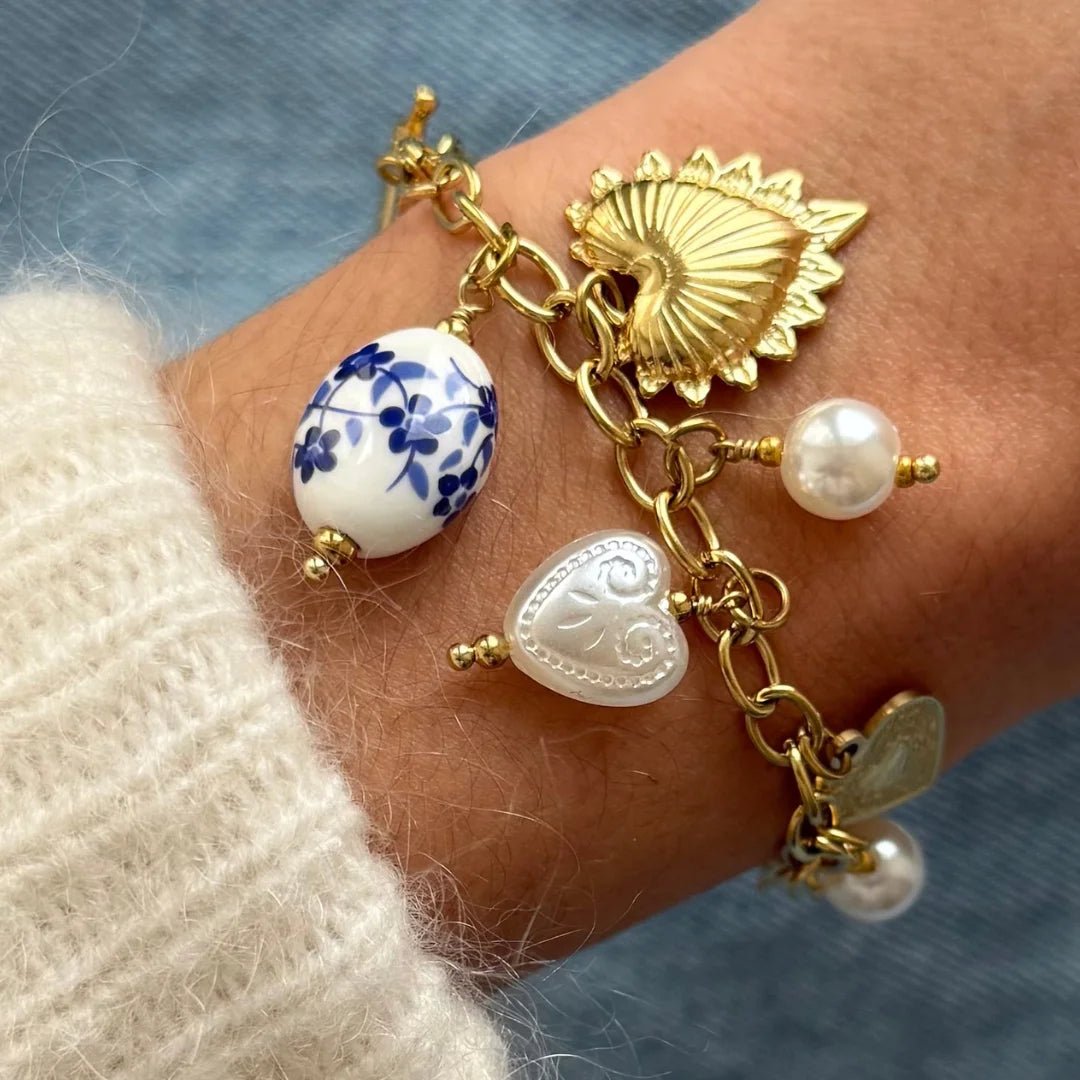 Gros plan bracelet chaîne à breloques : cœur sacré ex-voto, perle céramique bleue et perles nacrées sur acier doré.